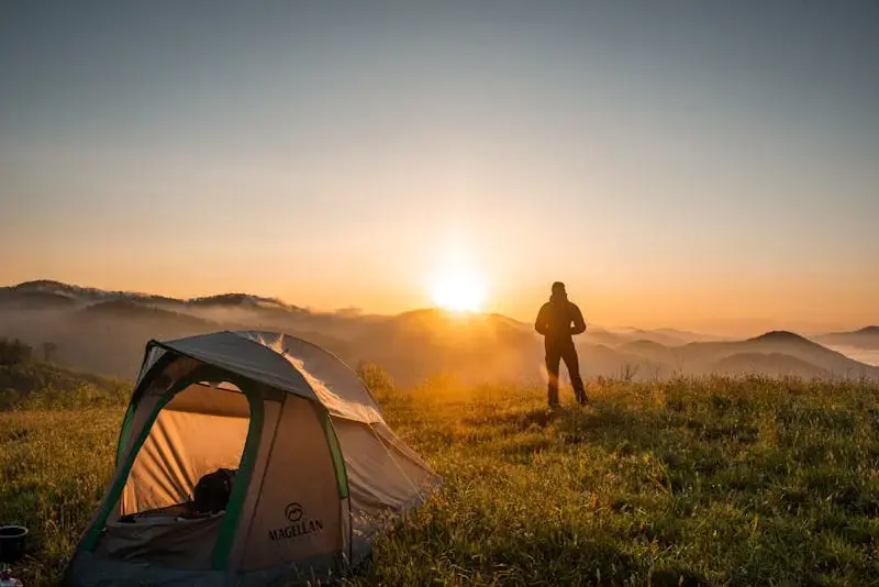 A camper enjoys sunrise in a mountain setting with a tent